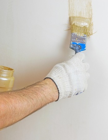 A hand in gloves puts a decorative paint brush. The concept of repair in the room.の写真素材