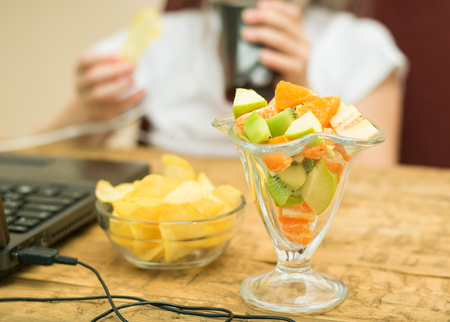 Tropical fruit salad and potato chips in front of a laptop. The child spends time at the computer.の写真素材