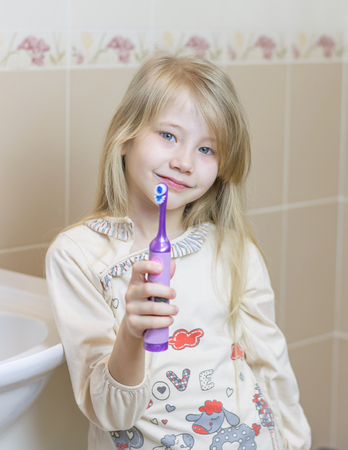 Beautiful girl shows an electric toothbrush in the bathroom. The concept of oral care.の写真素材