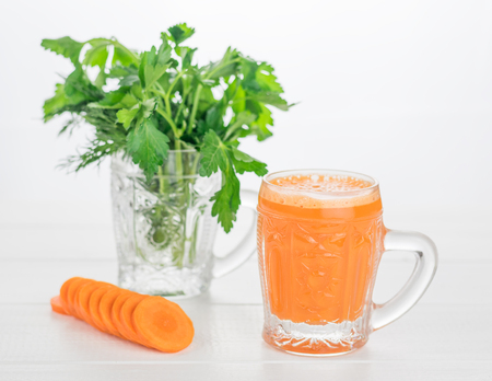 Carrot smoothies in a glass mug, dill and parsley on a white wooden table. Vegetarian concept of the kitchen for weight loss.の写真素材