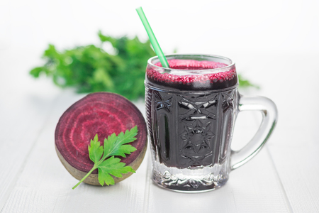 Half of the beets and beet juice in a glass mug on a white wooden table. The concept of a healthy vegetarian diet.の写真素材