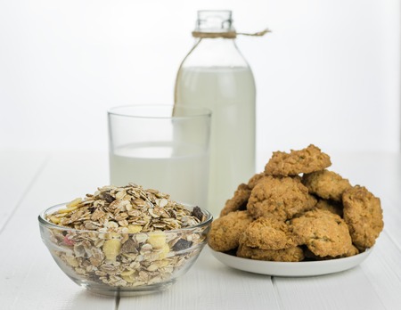 Milk bottle, bowl with muesli and fresh baked cookies on a white wooden table. Homemade cakes on wooden rustic table.の写真素材