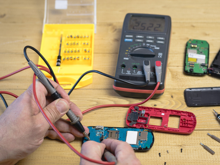 The person performs repair mobile phone on a wooden table. The concept of mobile phone repair.の写真素材