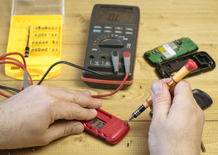 The person performs repair mobile phone on a wooden table. The concept of mobile phone repair.