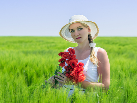 Woman with poppy flowers in field of green rye. Beautiful summer landscape.の写真素材
