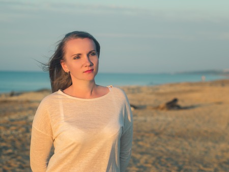 Beautiful woman on a sandy beach at sunset. Portrait of a beautiful woman by the ocean.の写真素材