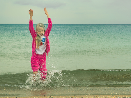 The girl in a warm suit plays in the cold sea. Child having fun on the ocean.の写真素材