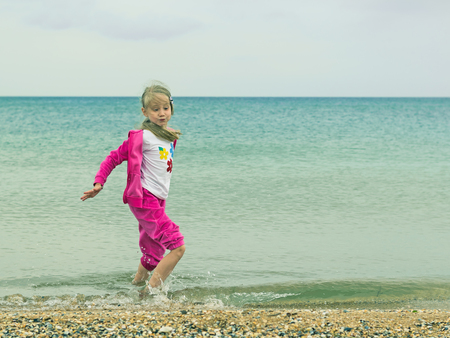 The girl in a warm suit plays in the cold sea. Child having fun on the ocean.の写真素材