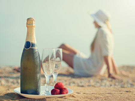 A bottle of sparkling wine with glasses on a white plate. Sandy summer beach in the sun.の写真素材