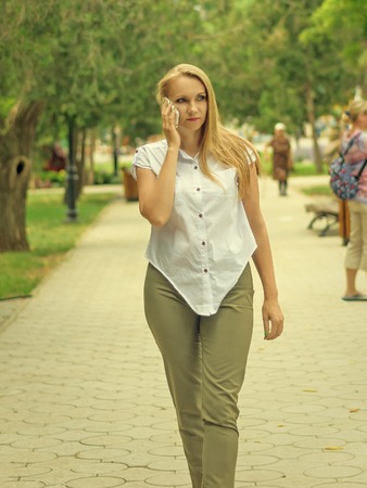Woman talking on mobile phone walking in the city Park. Beautiful woman hands with smart phone.の写真素材