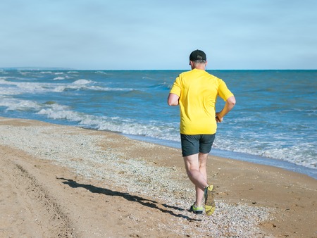 The man in the yellow shirt performs a morning jog on the beach. Sports in the open air by the sea.の写真素材