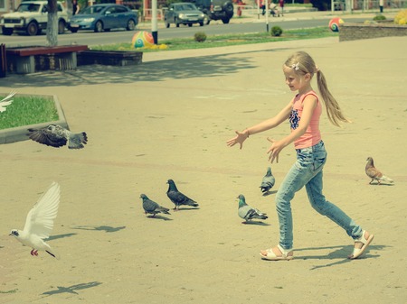 A girl is playing with pigeons in the town square. A child is entertained playing with birds.の写真素材