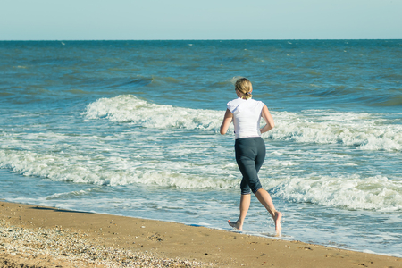 A woman in a white sports jacket is Jogging on the beach. The concept of a healthy lifestyle in nature.の写真素材