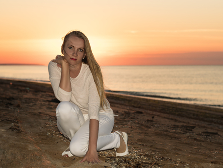 Woman in white dress on a sandy beach at sunset. Portrait of beautiful woman at sunset on the coast.の写真素材