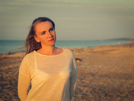 Beautiful woman in white clothes enjoying the sunset on the beach. Portrait of a beautiful woman by the sea.の写真素材