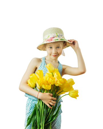 Beautiful girl in hat playing with yellow tulips isolated on a white background. The concept of a happy childhood.の写真素材
