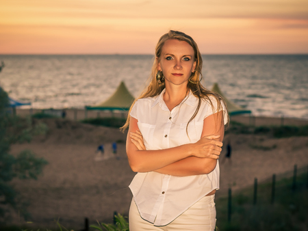 Beautiful woman in white clothes enjoying the sunset on the beach. Portrait of a beautiful woman by the sea.の写真素材