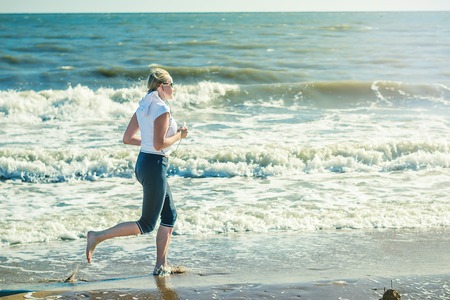 A woman in a white sports jacket is Jogging on the beach. The concept of a healthy lifestyle in nature.の写真素材