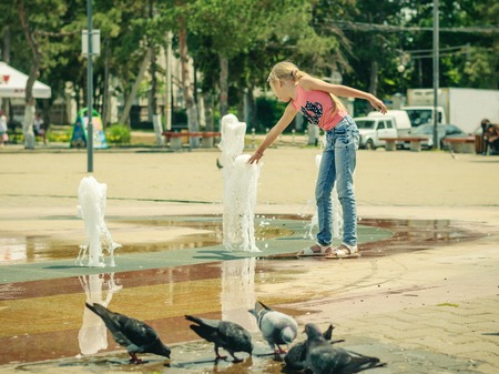 Little girl playing with water in city fountain. The concept of happy children's day in the sun.の写真素材