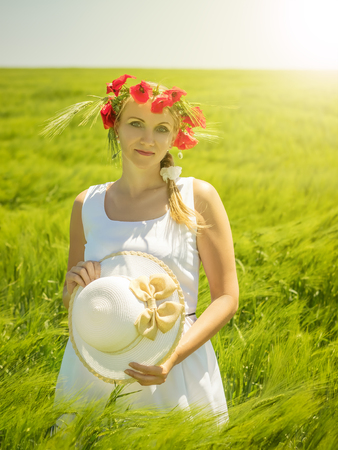 Beautiful woman with flowers poppies on the head in a field of green rye. Portrait of a beautiful woman on a background of green fields.の写真素材
