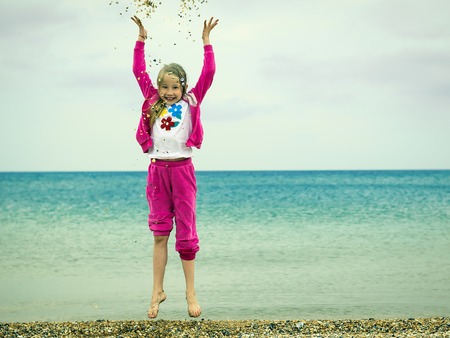 Cheerful girl in a warm suit plays with water in a cold sea. The concept of a happy childhood on the ocean.の写真素材