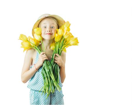 Beautiful girl in hat playing with yellow tulips isolated on a white background. The concept of a happy childhood.の写真素材