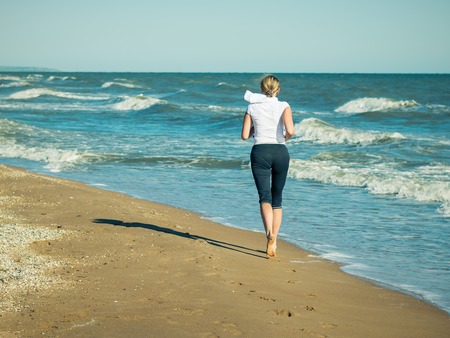 A woman in a white sports jacket is Jogging on the beach.の写真素材