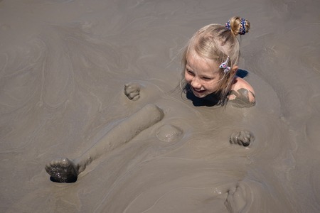 A little girl receives medical treatments in a mud volcano. Treatment of diseases using alternative medicine.の写真素材
