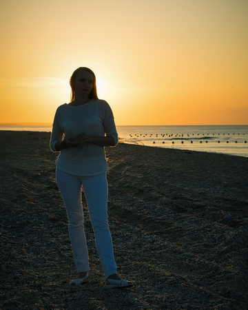 Beautiful woman in white clothes enjoying the sunset on the beach. Portrait of a beautiful woman by the sea.の写真素材