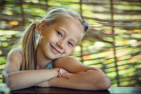 Portrait of a beautiful cheerful girl on a background of a fence of branches. The concept of a happy childhood.の写真素材