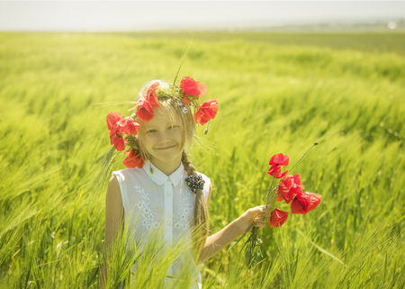 Cheerful beautiful girl with a bouquet of poppies in a field of green rye. The concept of a happy healthy childhood.の写真素材