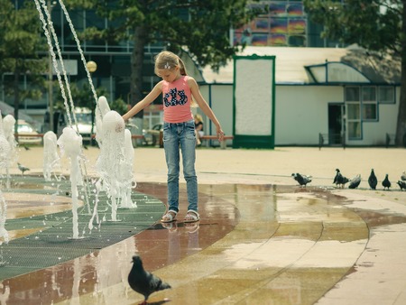 Little girl playing with water in city fountain. The concept of happy children's day in the sun.の写真素材
