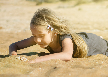 Little girl in gray dress is resting on the hot sand. The concept of a happy childhood in the summer.の写真素材