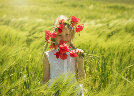Cheerful beautiful girl with a bouquet of poppies in a field of green rye. The concept of a happy healthy childhood.の写真素材