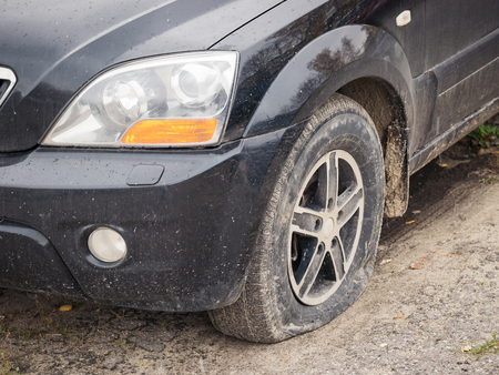 A black car with a deflated front wheel. Puncture of the left front wheel of the car.の写真素材