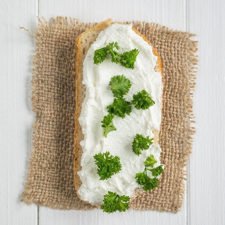 A fresh slice of bread smeared with cottage cheese cream with parsley on the table. The concept of a healthy diet.の写真素材