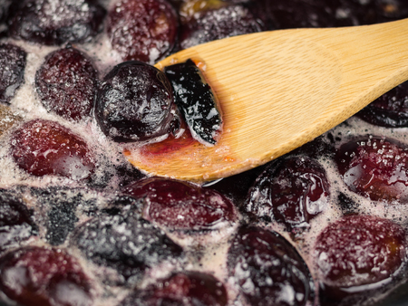 Ripe plums are cooked in sugar syrup and mix with a wooden spoon. The process of making plum jam at home.の写真素材