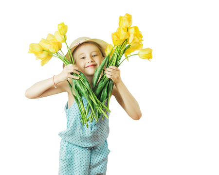 Beautiful girl in hat playing with yellow tulips isolated on a white background. The concept of a happy childhood.の写真素材
