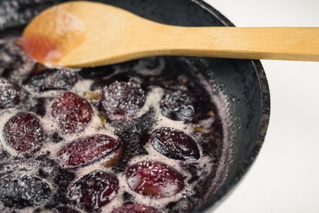 Ripe plums are cooked in sugar syrup and mix with a wooden spoon. The process of making plum jam at home.の写真素材