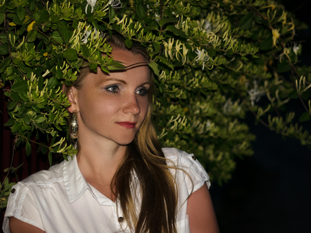 Portrait of a beautiful woman next to a flowering Bush at night. Woman in a white night shirt with flowers.の写真素材