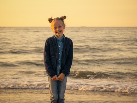 Girl with an interesting hairdo at the evening beach. Portrait of beautiful girl in jeans clothes on the seafront in the evening.の写真素材
