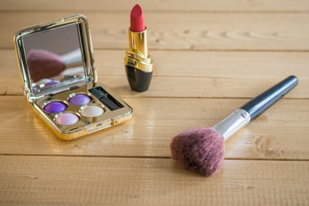 Makeup brush, lipstick and eyeshadow on a vintage table.の写真素材