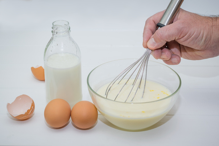 Male hand dunks a piece of white bread in milk-egg mixture. Preparation of toasted French bread.の写真素材