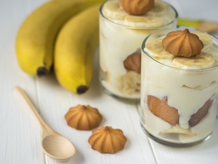 Two glass cups with banana pudding and wooden spoon on a white table. Milk and banana dessert. The concept of dietary vegetarian diet.の写真素材