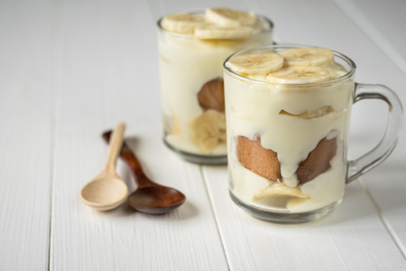 Two glass cups with banana pudding and wooden spoon on a white tableの写真素材