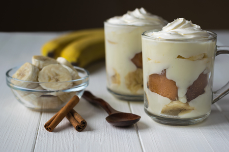 Two glass cups with banana pudding and wooden spoon on a white table. Milk and banana dessertの写真素材