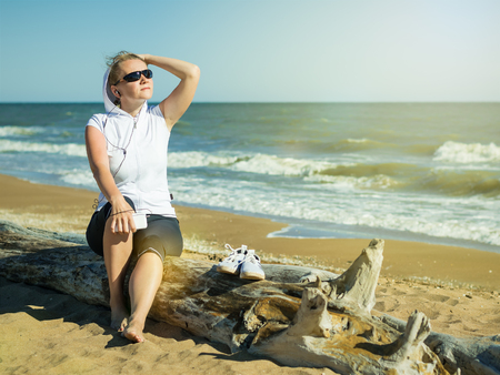 Woman in sportswear on a log at the beach. Morning sun after a workout.の写真素材