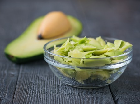 The flesh of the avocado in a glass bowl on a wooden table with a spoon. Vegetarian food. The concept of a healthy lifestyle.の写真素材