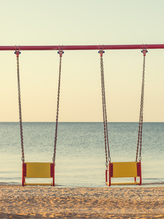 Swings on chains for two on the background of evening sunset sea. The concept of a romantic evening for lovers.の写真素材