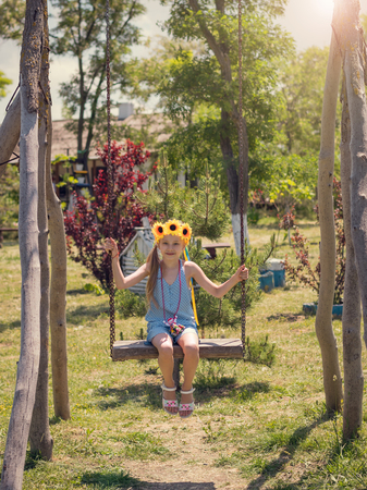Beautiful girl in the rays of the sun with the decoration of flowers on her head on the old swing. . The attraction of the past.の写真素材